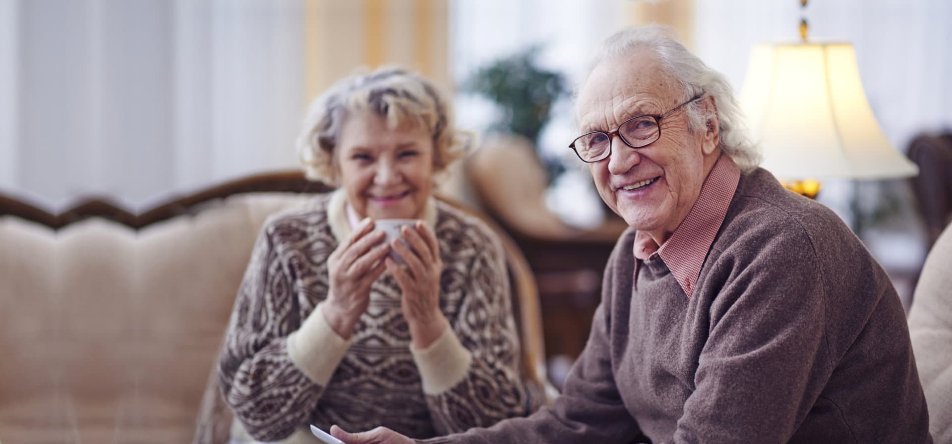 elderly couple sipping tea smiling in front of the camera